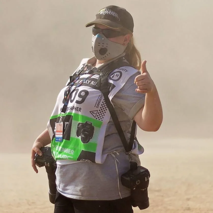 Motorsport photographer standing in a dusty event area